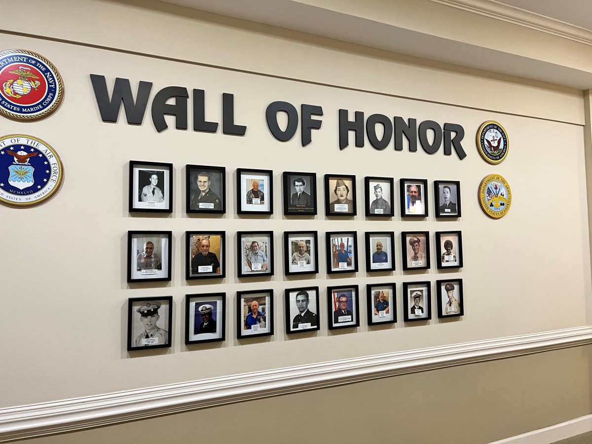 A Wall of Honor featuring framed portraits and military symbols displayed on a beige wall.