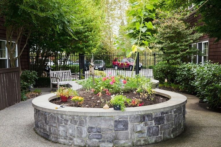 A peaceful garden with colorful flowers surrounded by a stone wall and benches.