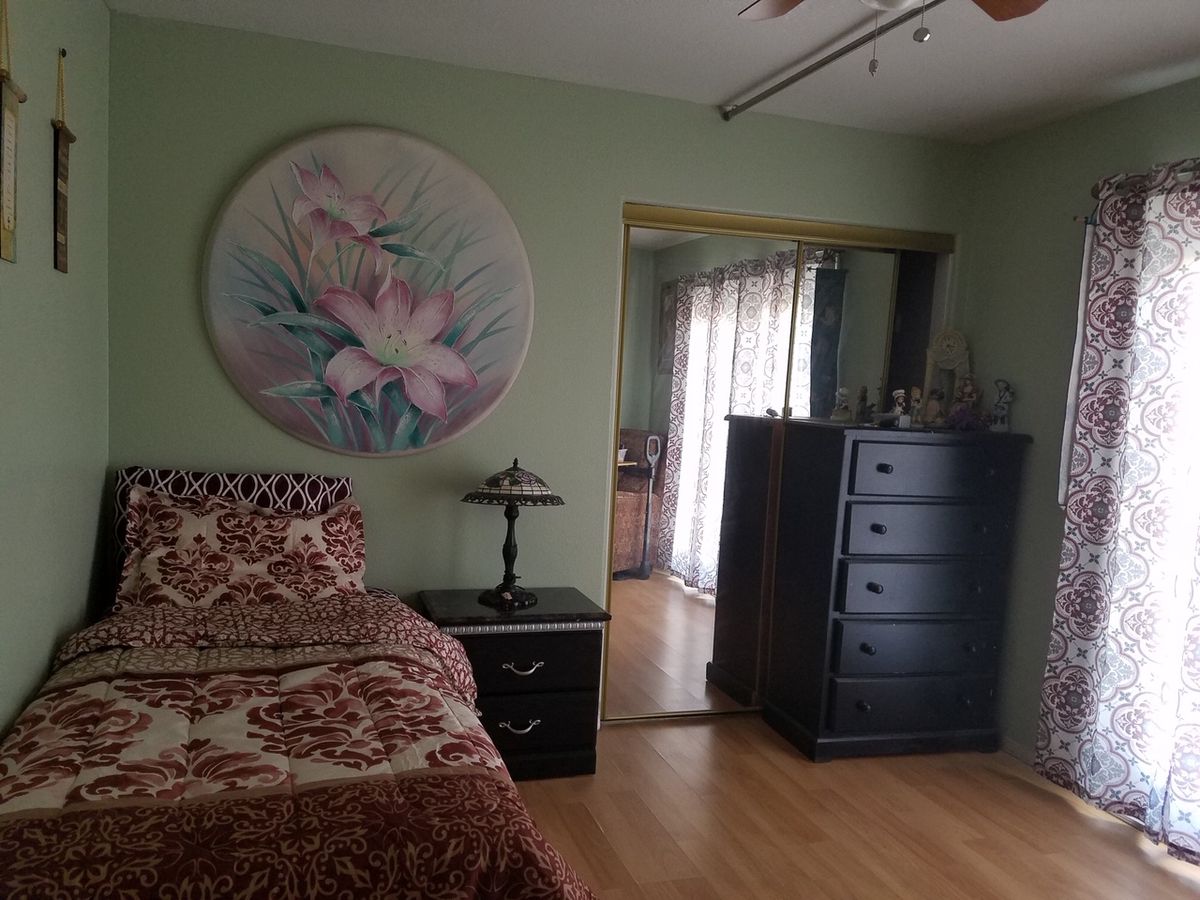 A cozy bedroom with a floral artwork on the wall, featuring a bed, nightstand, and dresser.