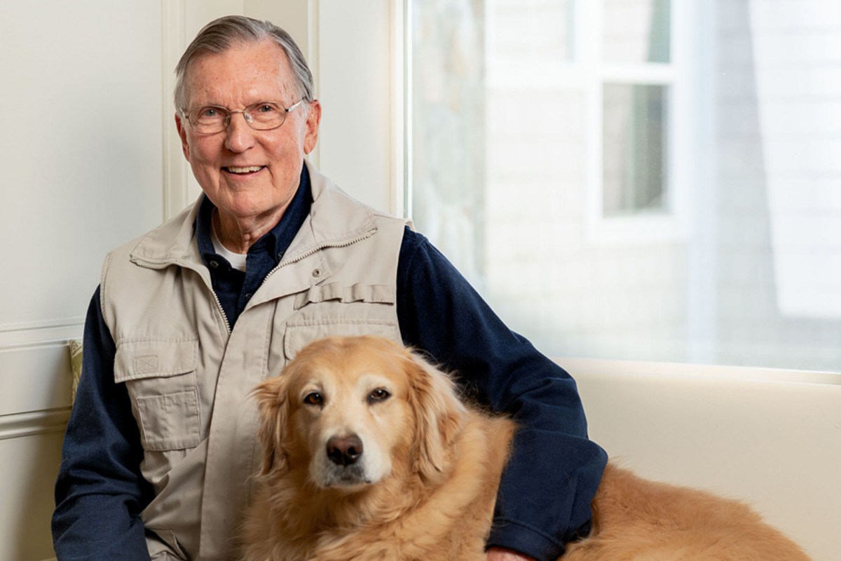 A man smiling while sitting next to his golden retriever indoors.