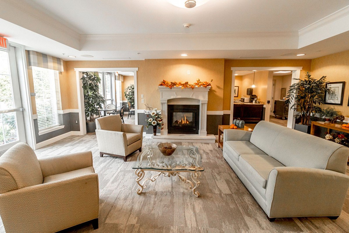 A cozy living room with a fireplace, sofas, and armchairs arranged around a glass coffee table.