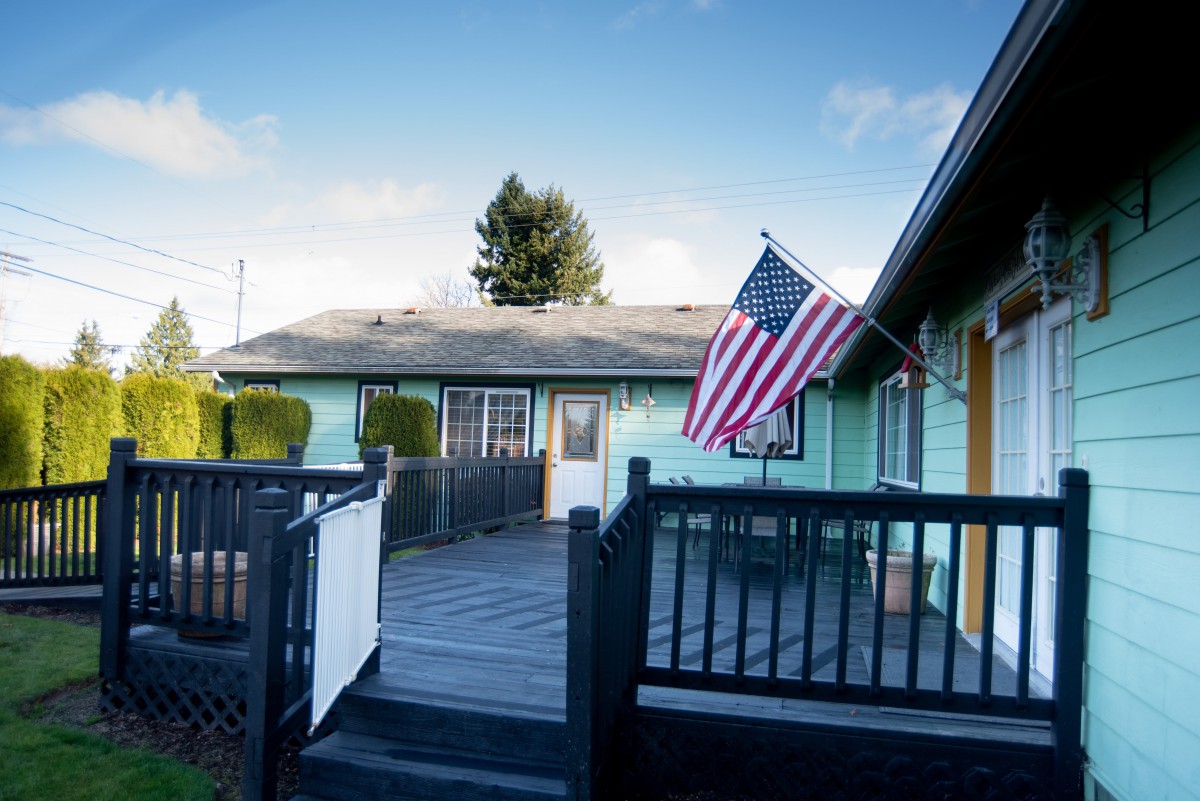A residential house with an American flag on display and a wooden patio under a clear blue sky.