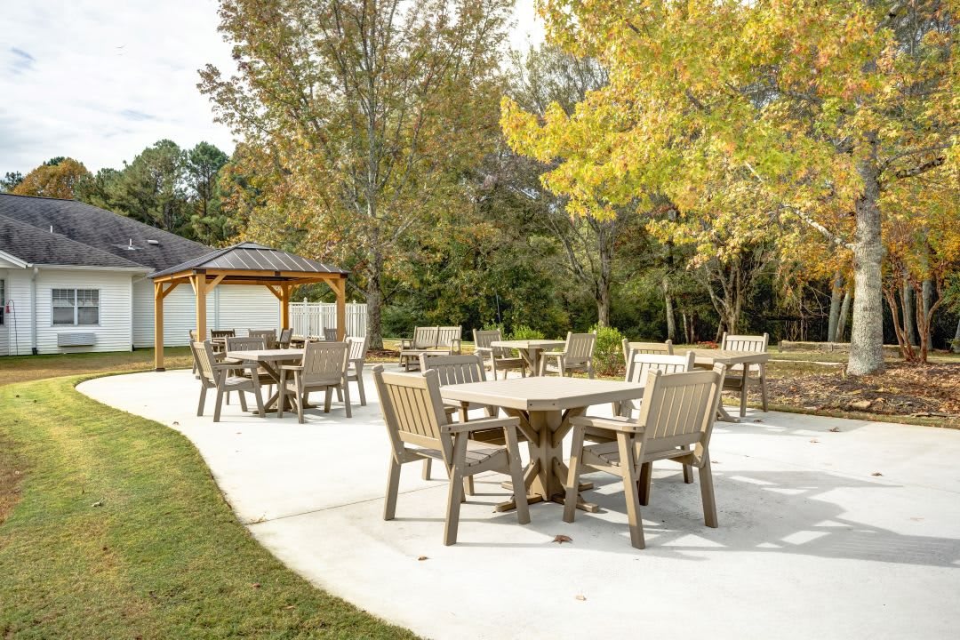 An outdoor patio area featuring wooden tables and chairs surrounded by autumn trees, with a gazebo in the background.
