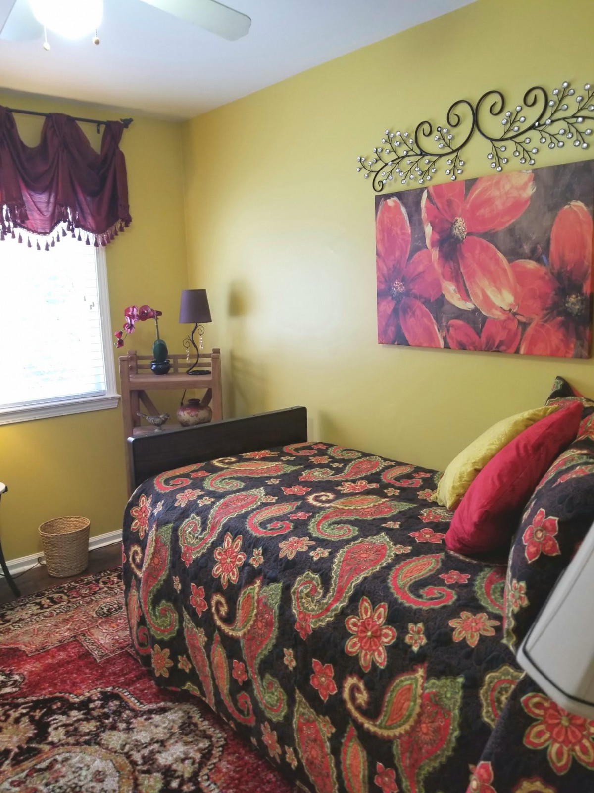 A colorful bedroom with floral decorations, featuring a single bed and artwork on the wall.