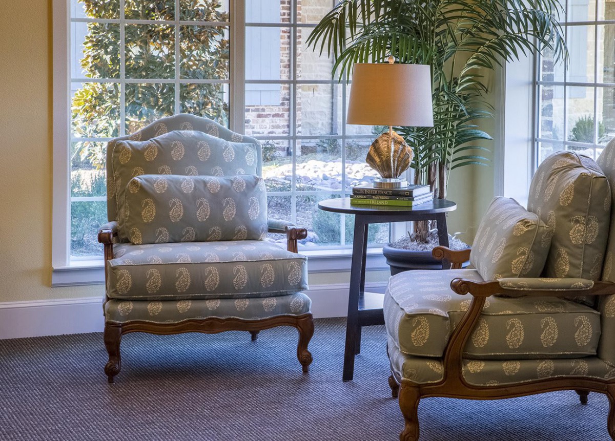 A cozy living room corner with elegant chairs, a side table, and a decorative lamp near a large window.