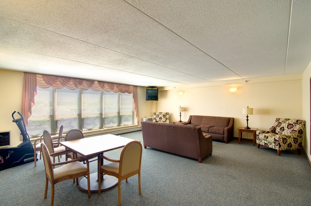 A spacious living room with large windows, featuring a sofa, table, and chairs.