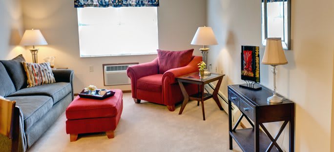 A cozy living room with a red armchair and ottoman, accompanied by a side table and lamp beside a television.