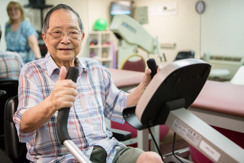 An elderly man exercising on fitness equipment in a gym setting.