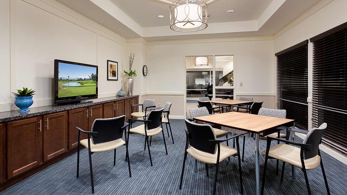 A modern meeting room with tables, chairs, and a television.