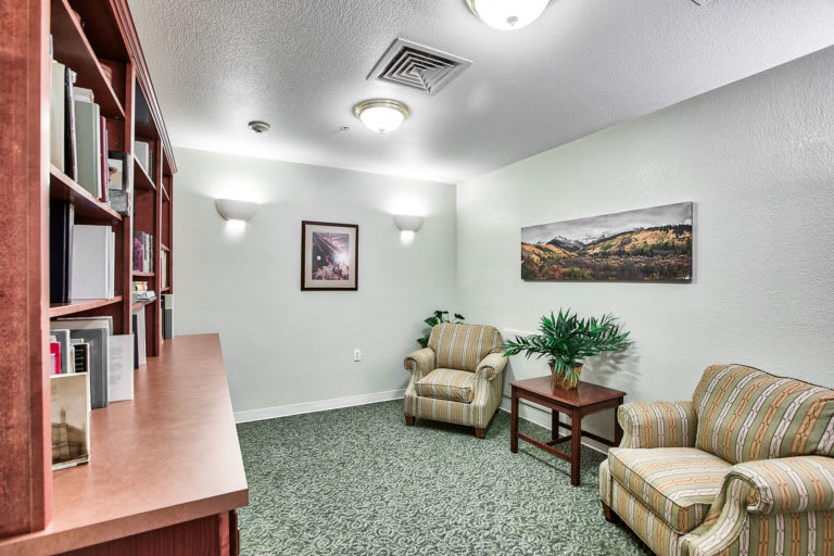A cozy waiting room with comfortable chairs, a side table, indoor plants, and framed artwork on the walls.