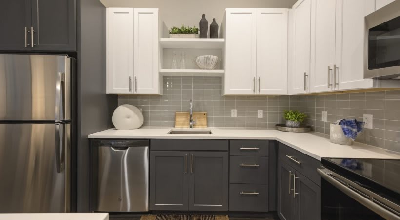 A modern kitchen with white upper cabinets, dark lower cabinets, and stainless steel appliances.