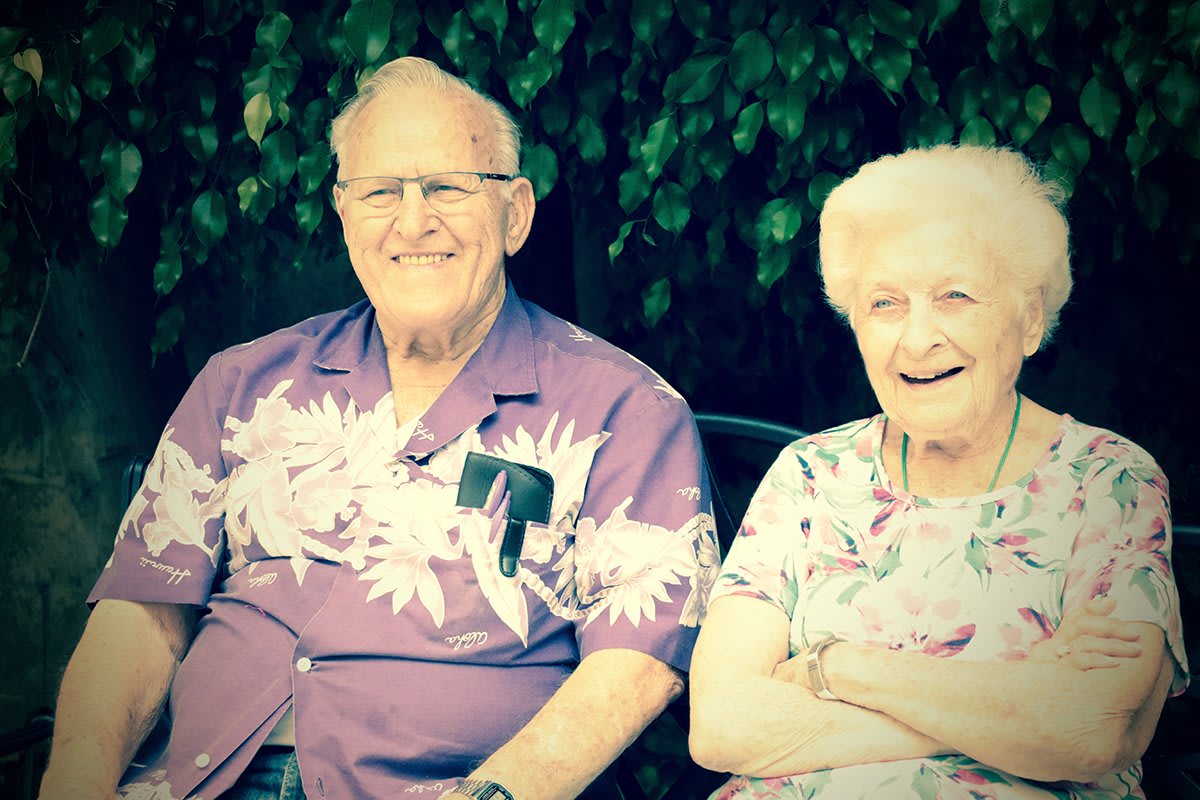 An elderly couple smiling while sitting together outdoors.