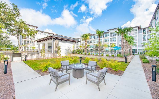 A sunny day view of a modern apartment complex with an inviting outdoor patio area and lush garden.