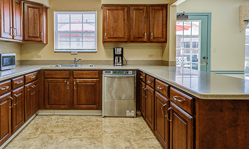 A modern kitchen with wooden cabinets, a coffee maker, and a tiled floor.