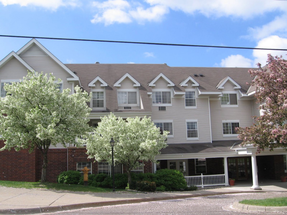 A multi-story residential building with trees in front, set against a blue sky.