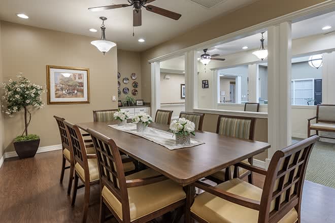 A well-furnished dining room featuring a long wooden table surrounded by chairs, with a chandelier and ceiling fans overhead.
