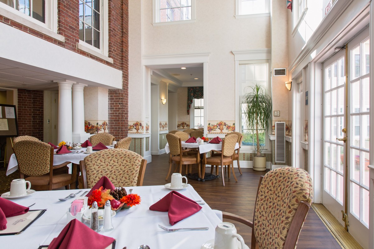 A well-lit restaurant dining area with tables neatly set for patrons, featuring elegant decor and large windows.