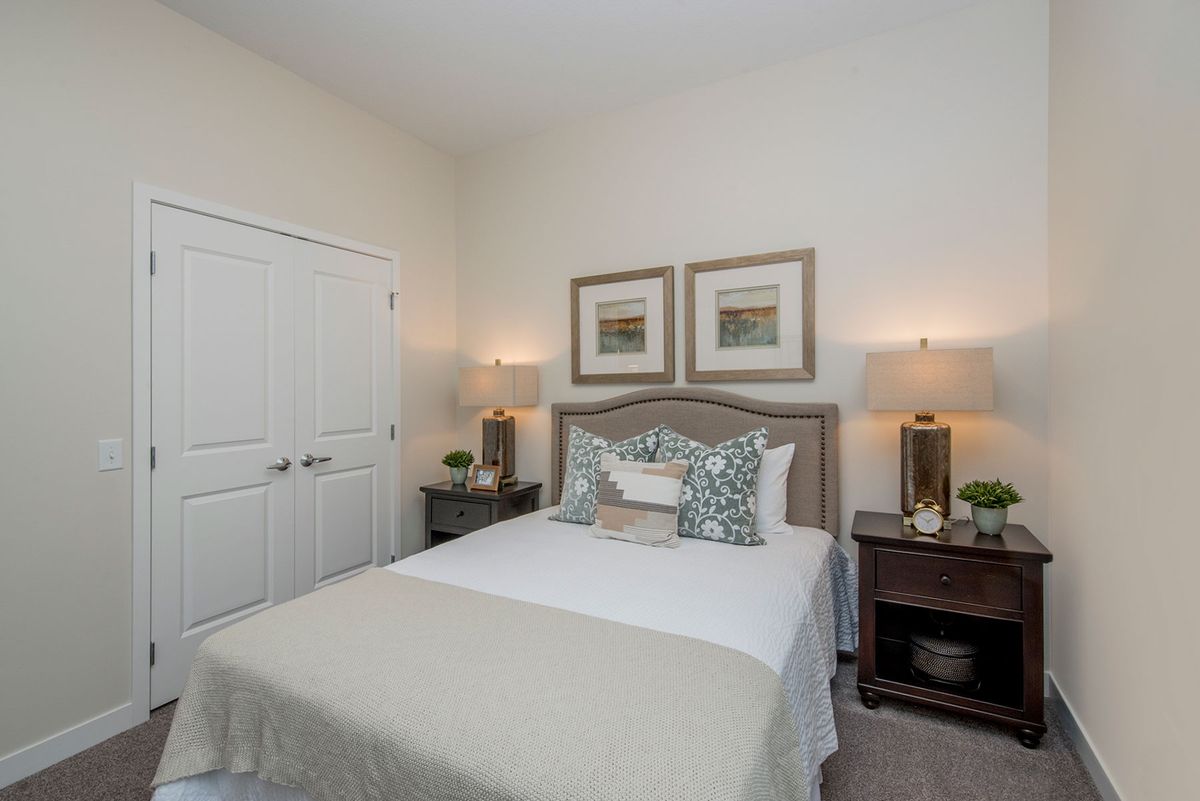 A cozy bedroom with a neatly made bed, matching nightstands and lamps, and framed artwork above the headboard.