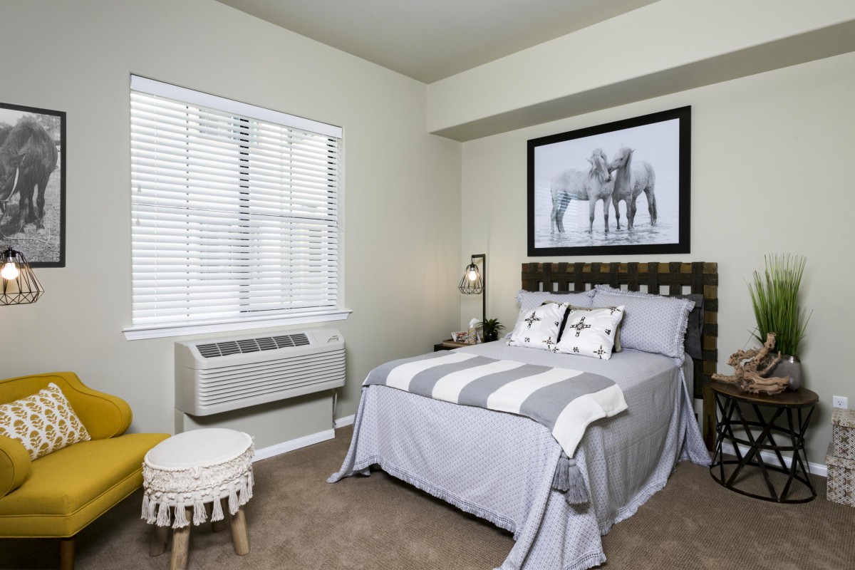 A modern bedroom featuring a neatly made bed, a large piece of artwork above the headboard, and a window with blinds.