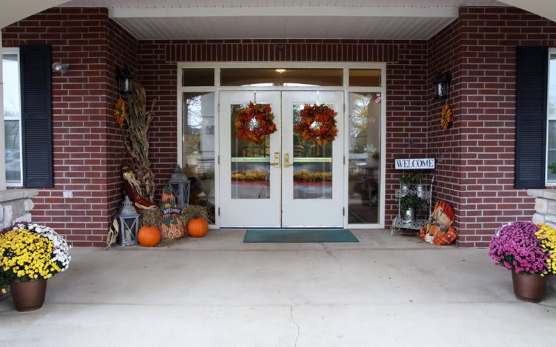 A front entrance decorated for autumn with pumpkins, wreaths, and seasonal decor.