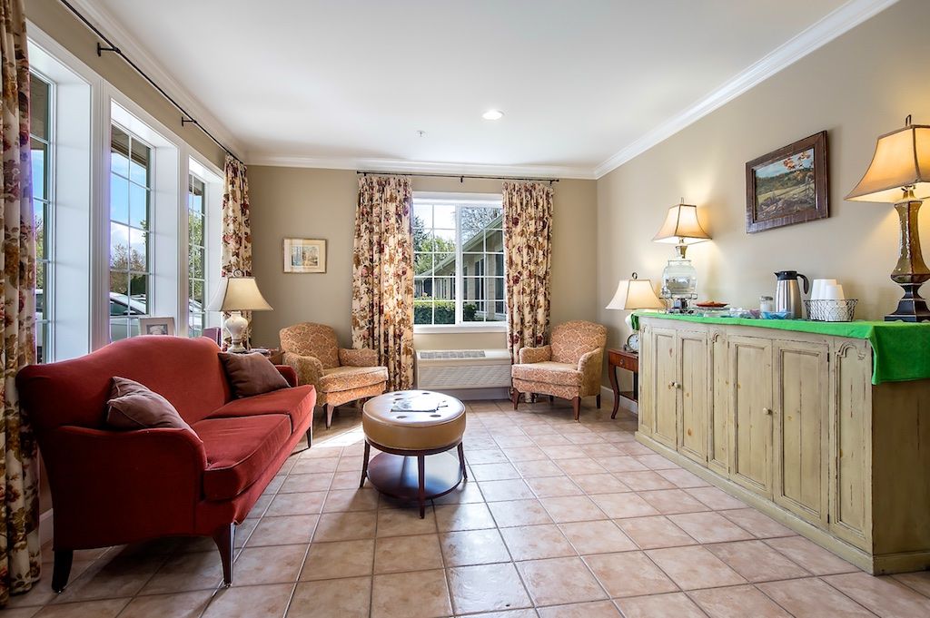 A cozy living room with a red sofa, armchairs, a round coffee table, and patterned curtains framing a large window.