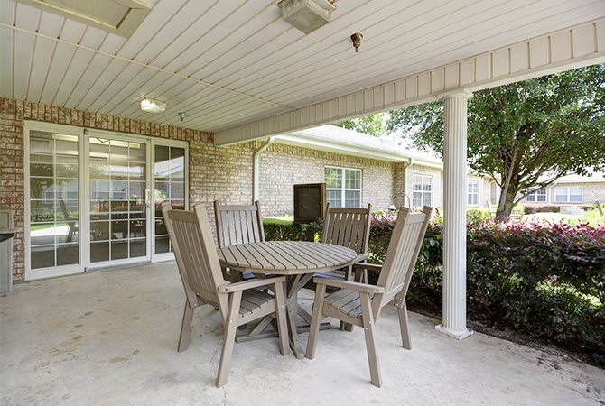 A covered patio area with a table and chairs overlooking a garden.