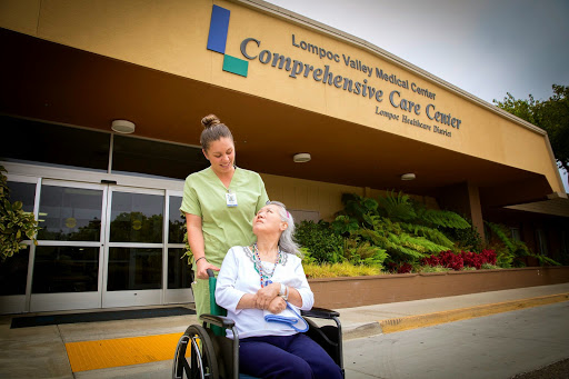 A healthcare worker assists an elderly patient in front of the Comprehensive Care Center.