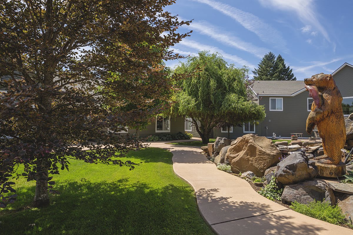 A well-landscaped garden with a pathway leading to a house, surrounded by lush greenery and rocks.