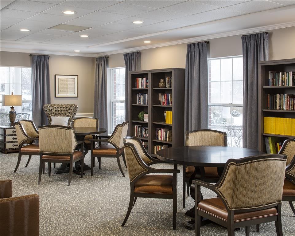 A cozy library room with bookshelves, tables, and chairs arranged for reading and relaxation.