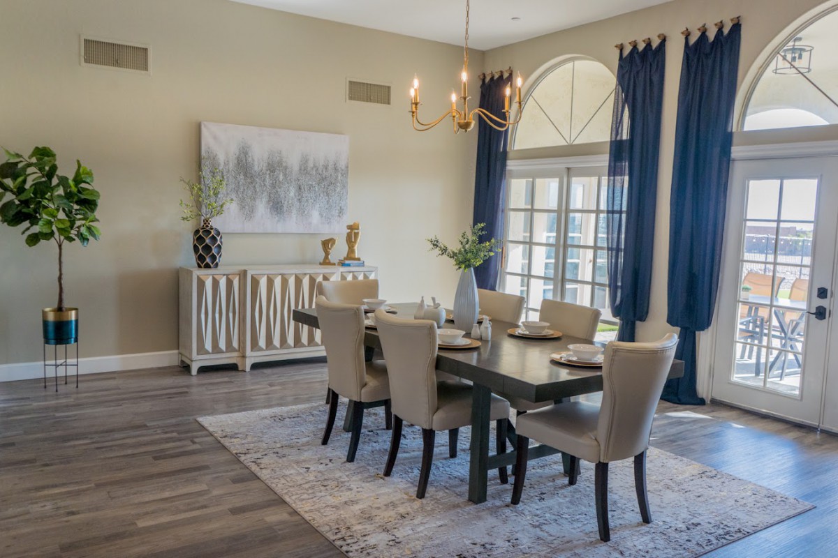 A modern dining room featuring an elegant chandelier, stylish table settings, and navy blue curtains.