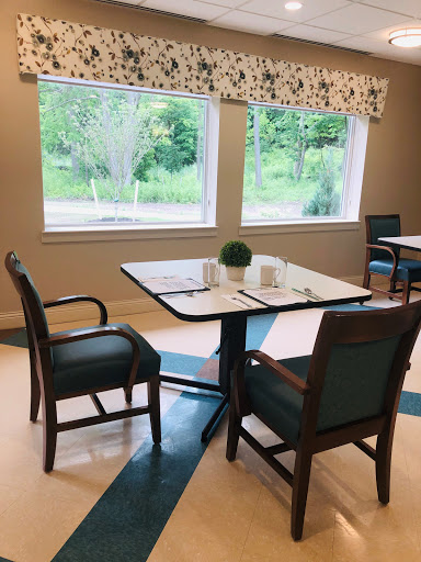 A cozy dining area with a table set for two, overlooking greenery through large windows.
