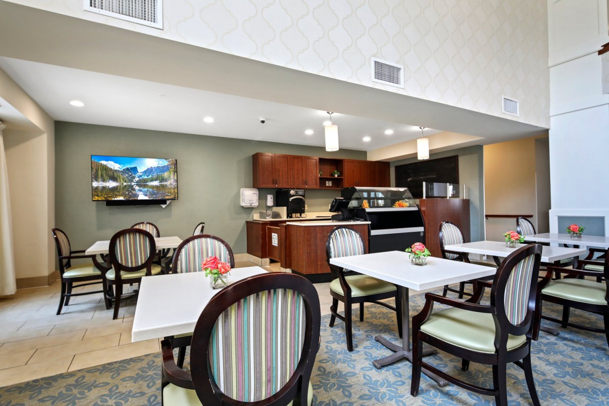 A modern dining area with tables and chairs, featuring a small kitchenette in the background.