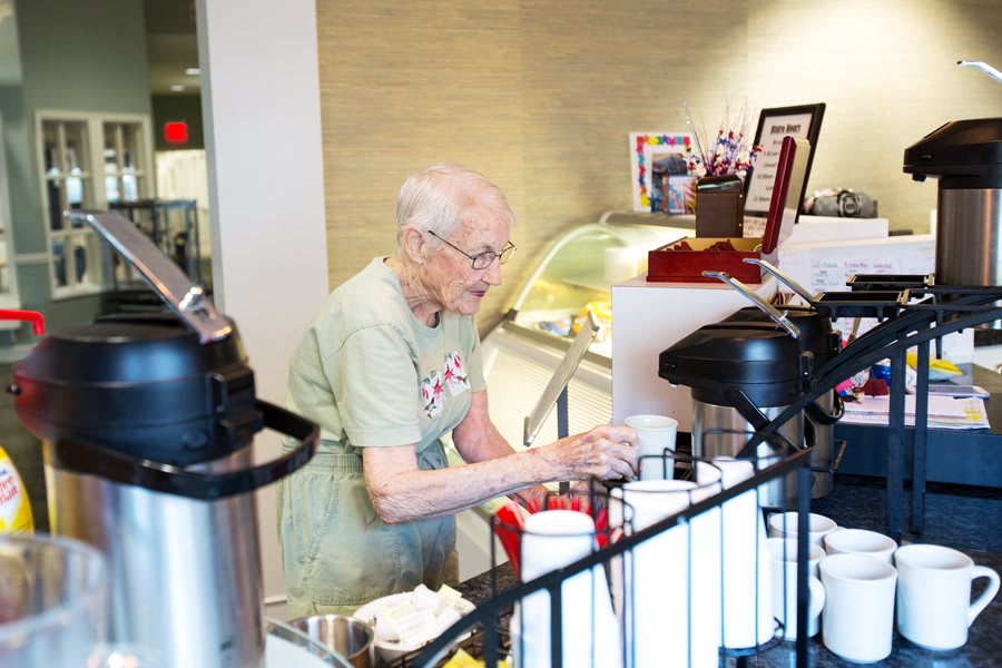 An elderly person serving coffee in a cafe.