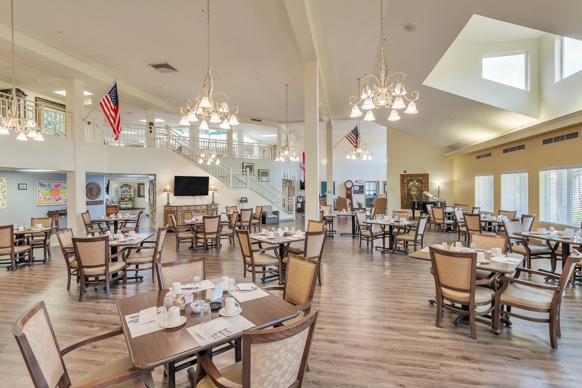 A spacious, elegantly decorated dining area with neatly arranged tables and chairs, featuring chandeliers and a wooden floor.