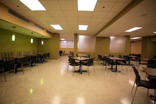 An empty modern dining area featuring round tables and chairs, illuminated by overhead lighting.