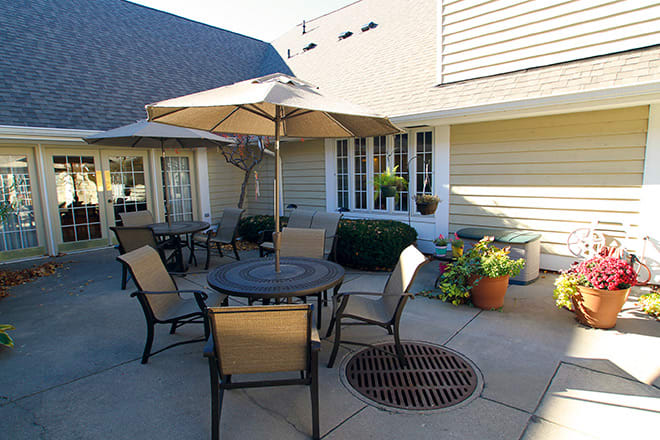 A sunny patio area with tables, chairs, and umbrellas beside a building.