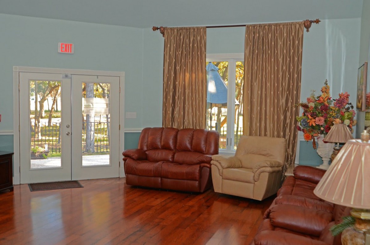 A cozy living room with leather sofas and armchairs, featuring large curtains and a wooden floor.