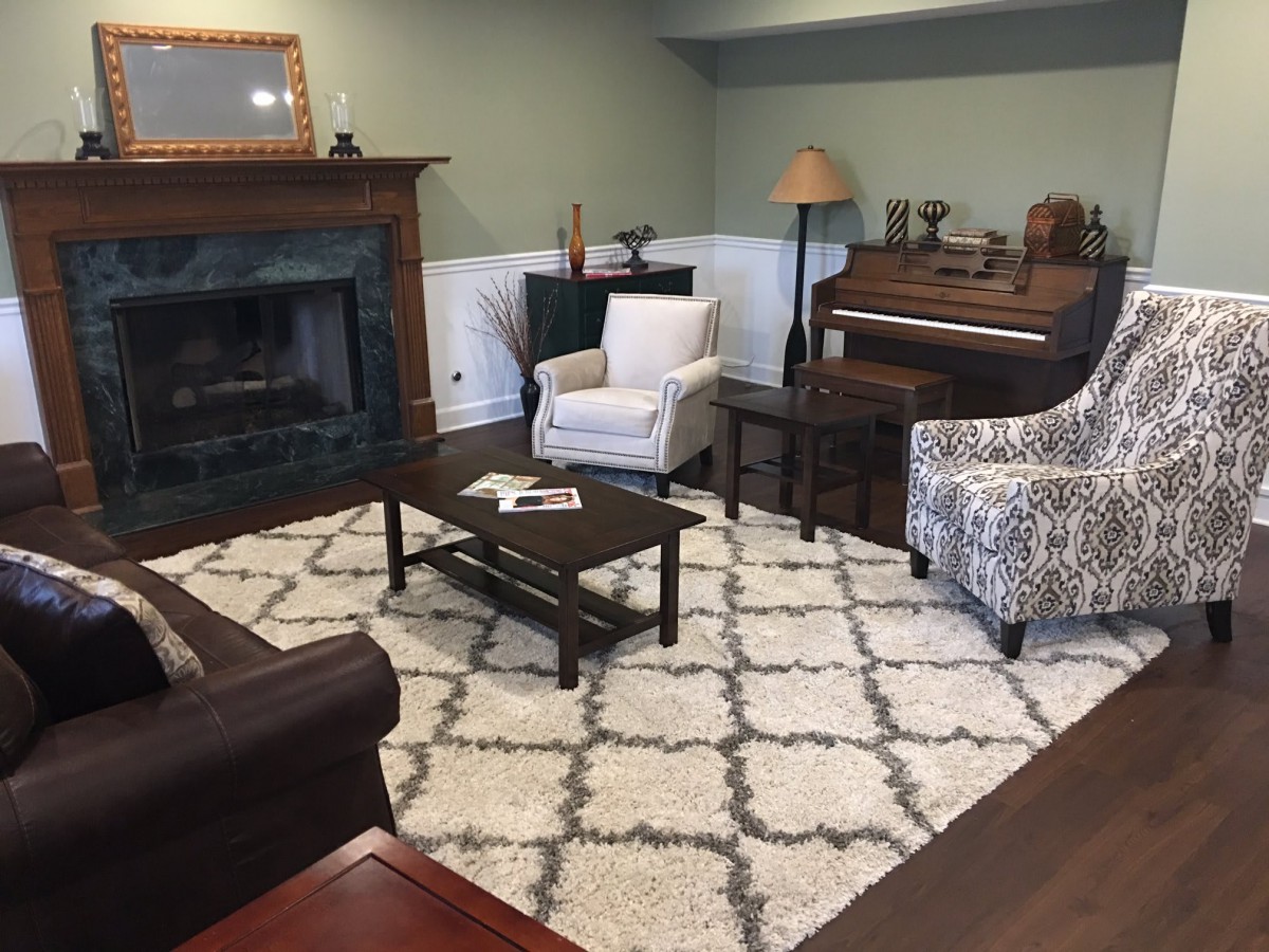 A cozy living room featuring a fireplace, armchairs, and a piano.