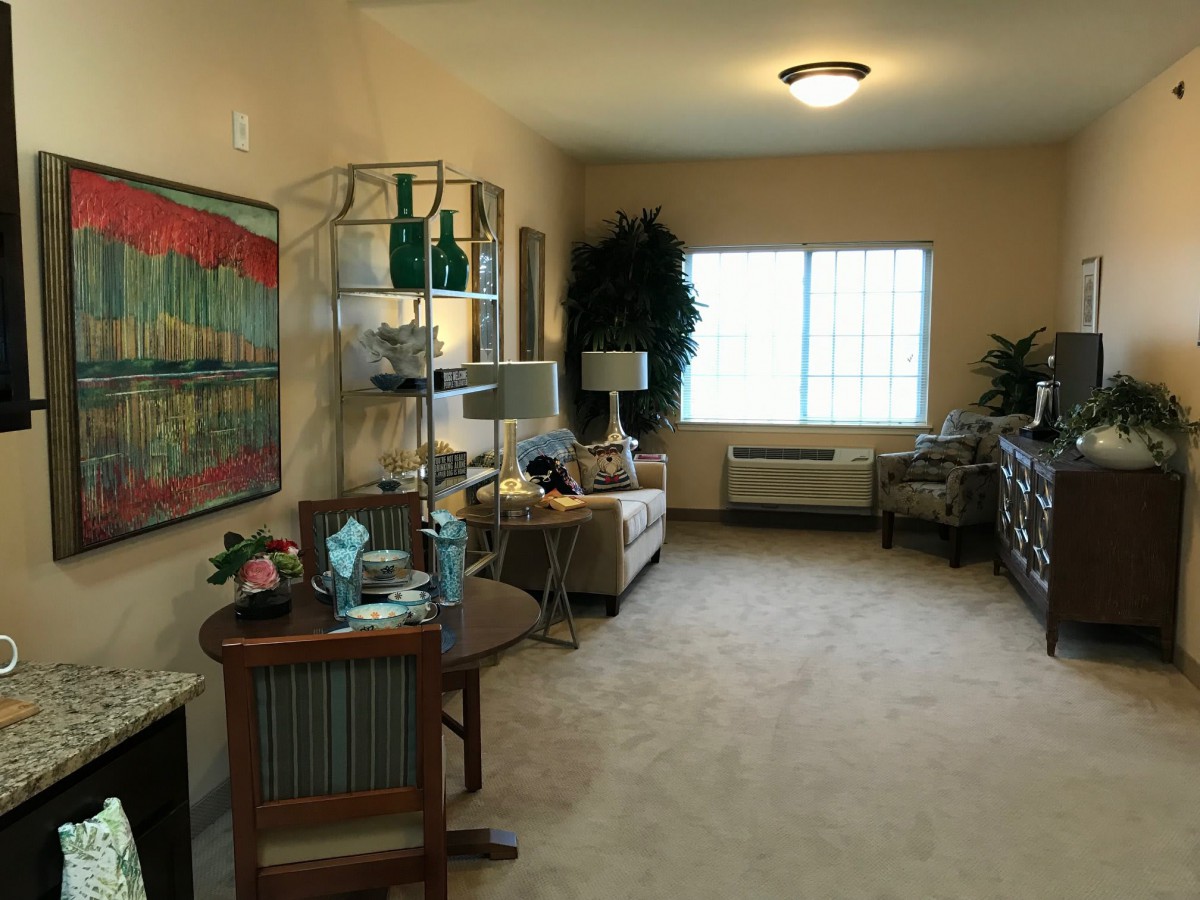 A cozy living room with tasteful decor, featuring a couch, decorative shelves, and a large window allowing natural light.