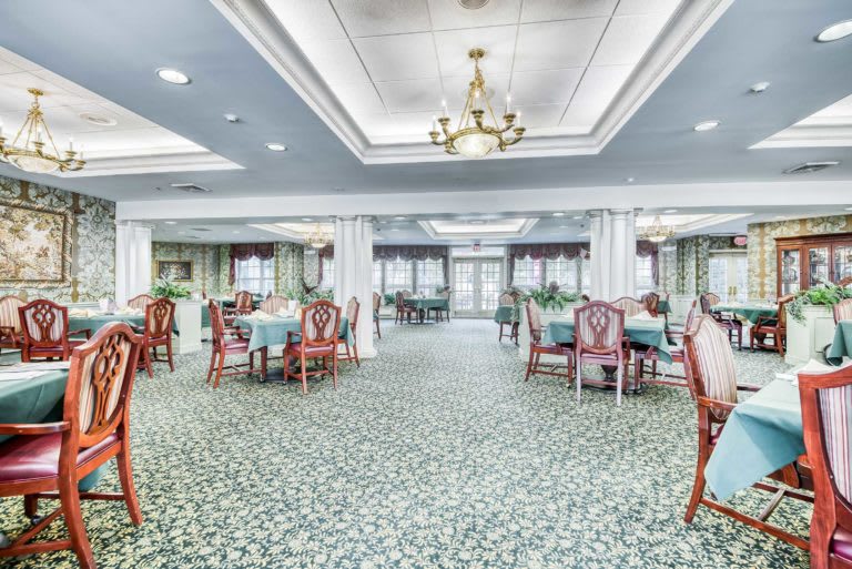 A spacious dining room with elegant decor, featuring multiple tables and a chandelier.