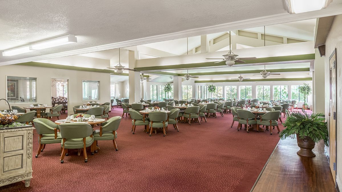 A spacious dining area with multiple tables and chairs, featuring large windows and ceiling fans.