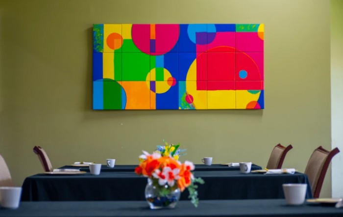 A colorful abstract painting hangs on the wall of a conference room, with a bouquet of flowers in a vase on the table.