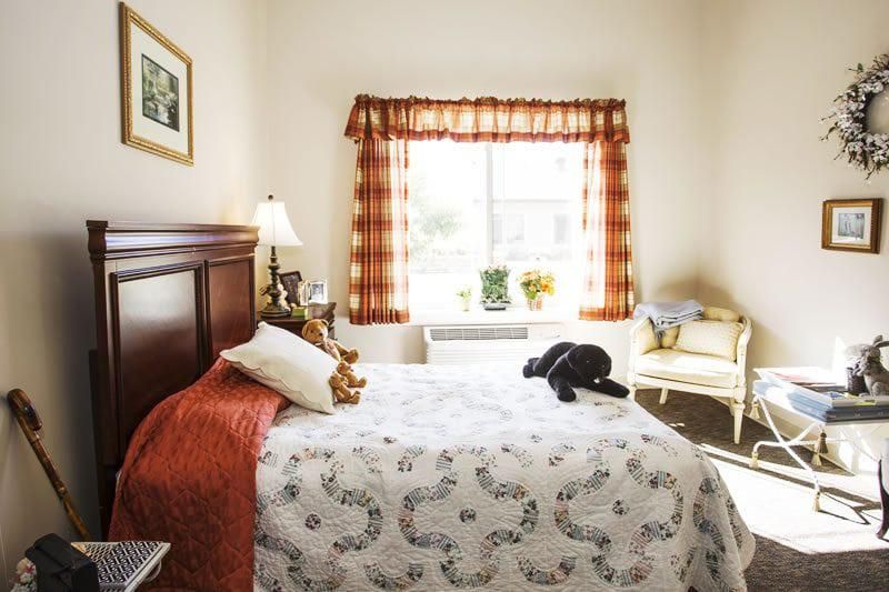 A cozy bedroom with a neatly made bed, allowing natural light in through a large window.