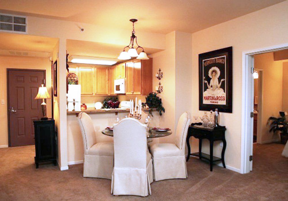 A cozy dining area with a small round table adjacent to a warm-lit kitchen, featuring elegant decor and wall art.