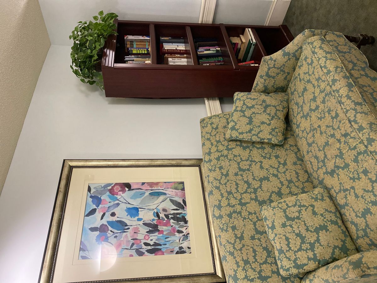 A cozy reading corner with a patterned sofa, bookshelf, and vibrant artwork.