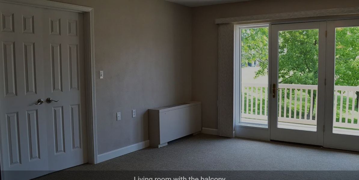 A bright, empty room with a large window and balcony view.