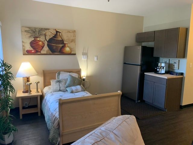 A cozy studio apartment with a single bed, kitchenette, and decorative artwork.