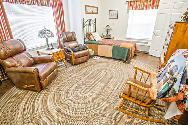 A cozy bedroom with a single bed, leather chairs, a rocking chair, and a braided rug.