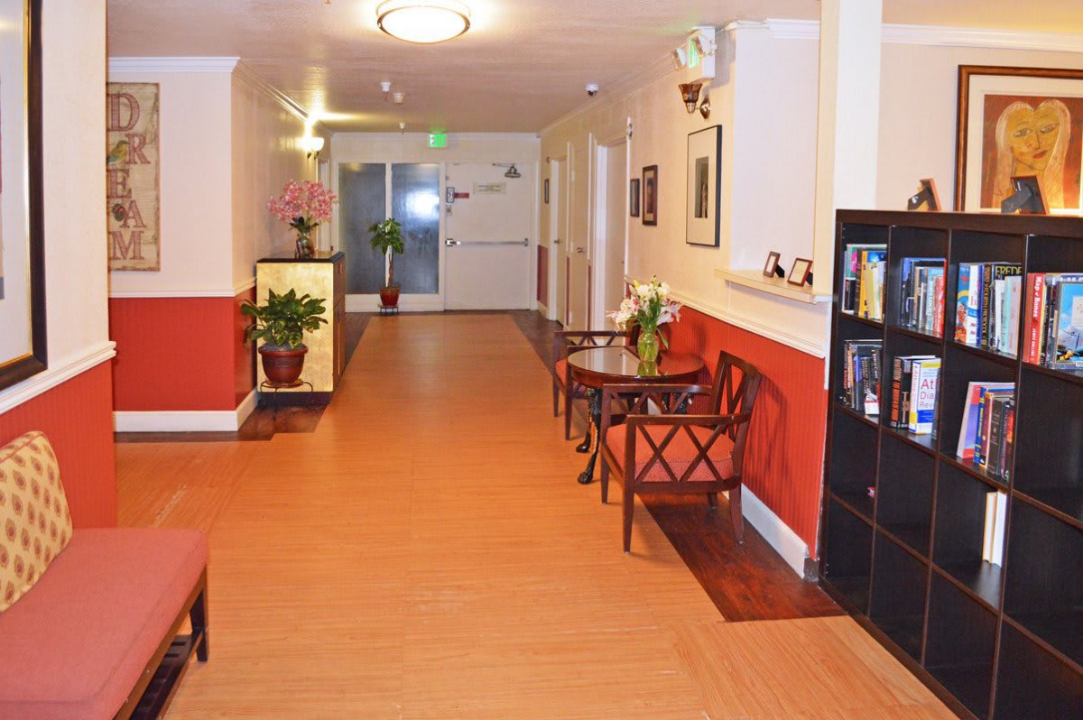 A well-decorated hallway with wooden flooring, featuring chairs, tables, and potted plants.