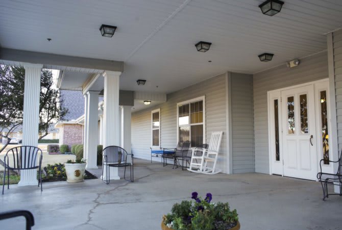 A building with a spacious porch featuring chairs and decorative columns.